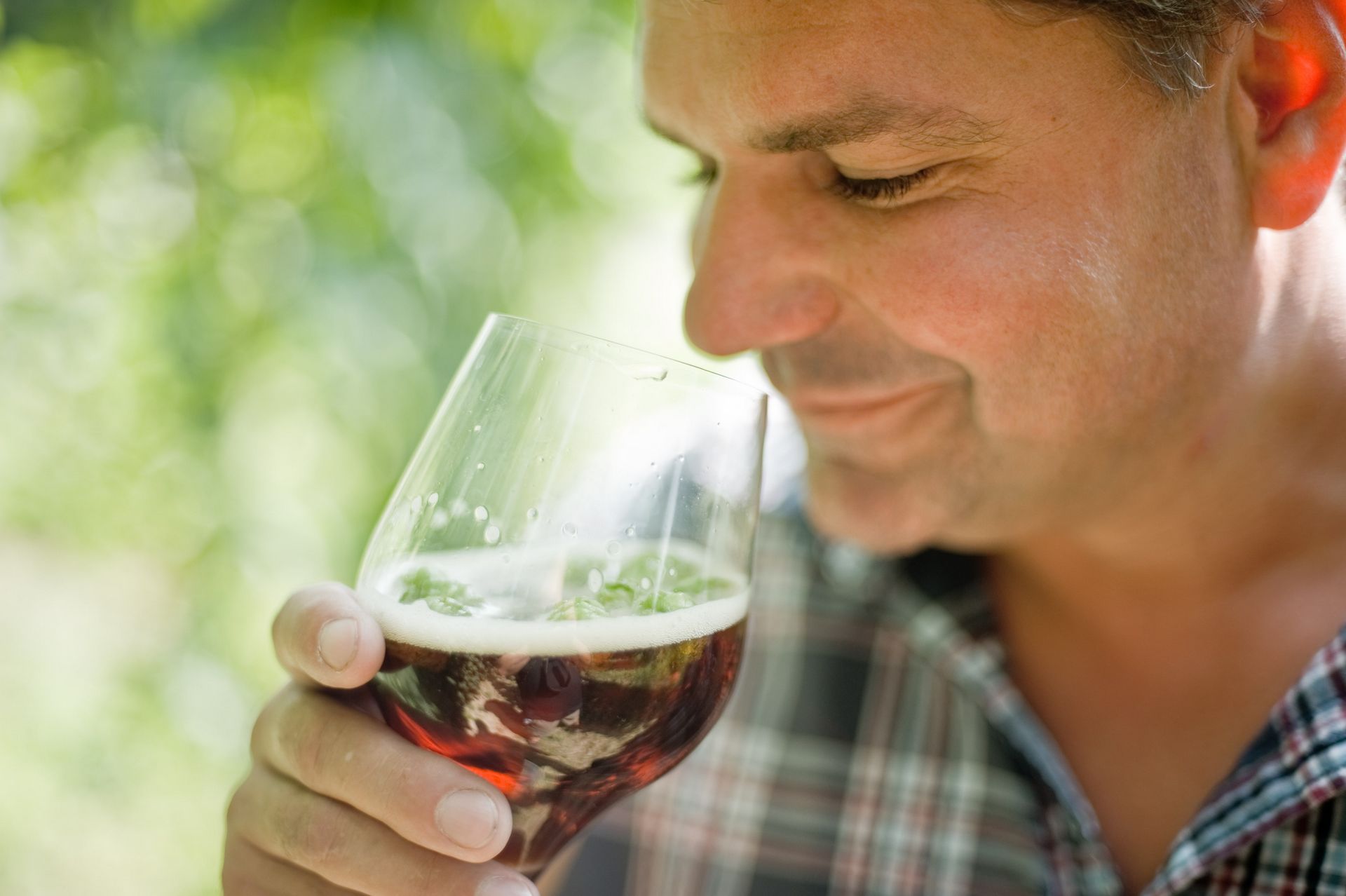 Man enjoying and smelling a glass of dark beer outdoors — used in a past web design project for Schlossbrauerei Au Hallertau, a traditional German brewery.